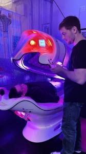 A serene image showcasing a person comfortably resting inside the Slimwell 360 Magic Cocoon, surrounded by gentle, colorful light. The soothing ambiance of the cocoon is enhanced by the therapeutic benefits of light therapy, hyperthermia, and comforting t