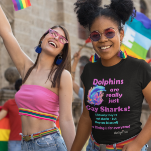 Picture at pride parade with two girls holding hands . One girls is wearing a Dive Cupid T-shirt that says "Dolphins are really just gay sharks, actually they are bisexual and born that way, Scuba Diving is for everyone, DiveCupid.com