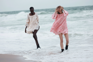 Models wearing pink and ivory short dresses by the shore