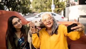 A happy family sits with a dog on an outdoor bench and poses for a picture together.
