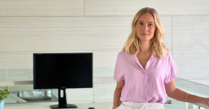Blond kvinna, grundare och VD för Iconica Wear, står självsäkert med ena handen i fickan, klädd i en rosa skjorta och tittar in i kameran
