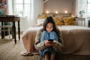 Teen girl sits on the floor in her room looking at her smartphone.