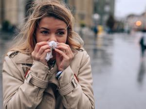 Young Queensland woman blowing her nose with a tissue.