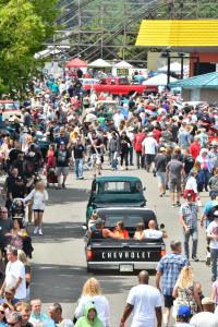 Classic vehicles cruise through a huge crowd during a Goodguys car show.