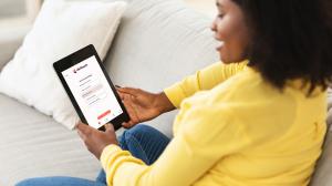 A woman in a yellow cardigan sat on a sofa using Clinitouch on a tablet device