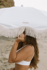 Photography of a Woman with dark hair hiding her face with a classy white beach umbrella
