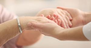 Caring adult female counselor holding elderly person's hands in support