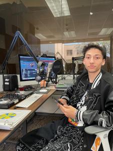 This is a picture of the music artist, Amani, inside a radio show studio, sitting down at a desk in front of a microphone.