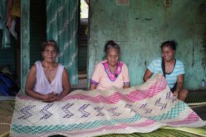 Three woman sitting with a traditional woven mat