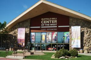 Photo of the facade of the Buffalo Bill Center of the West showing the entrance and names of the 5 museums, as well as two large vertical banners