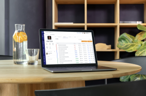 Laptop computer sits on a circular table in an office next to a water carafe with oranges.