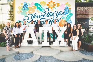 The 1836PM team gathered around a sign that says ATX.