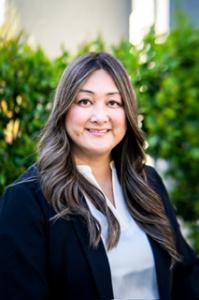 Mary Tran, the new CEO of EXP - the opportunity engine, stands outdoors against a backdrop of lush green foliage. She exudes professionalism and confidence, captured in her head-and-shoulders headshot. A warm smile graces her face, reflecting her leadersh