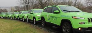 A fleet of green SUVs with Wound Care Plus logos on the side parked in a row on a treed street.