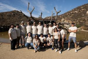 A group of 17 people are standing outside, huddled together and smiling.