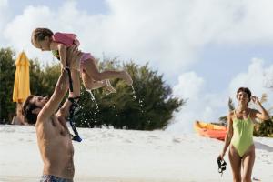  A man and woman play with a child on the beach during their Family Holiday at Cinnamon Hotels & Resorts.