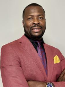 A photo portrait of a man in a black shirt with a bright maroon blazer and tie. 