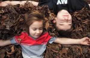 Two kids relax in fall leaf piles as Wondercide suggests flea and tick tips.