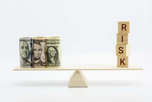 A teeter totter with three rolls of money on one side and blocks on the other side that spell out "RISK"