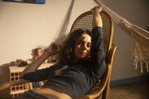 Woman sitting on a chair streaching. She has white skin, black long hair and wears a dark grey long sleeves.