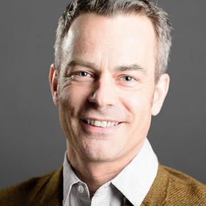 headshot of ben robertson wearing a brown tweed jacket and white, button collar shirt