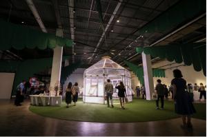 Visitors are viewing the exhibition artworks. The main artwork in this photo is the octagonal glass cabin with light from inside and coconut leaves-like structures extending in eight directions | Photo - AVING News