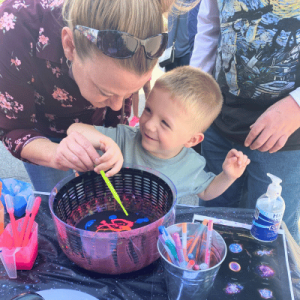 young boy at miSci event smiling as a woman helps him with activity at an outside display