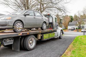 A grey sedan loaded onto a white flatbed tow truck