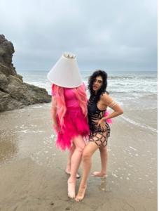 Farrah Mechael is wearing a black bathing suit one piece with cut outs. Shitty Princess is wearing a pink shirt and a short pink tutu with a white lampshade on her head with a sparkly crown on top.