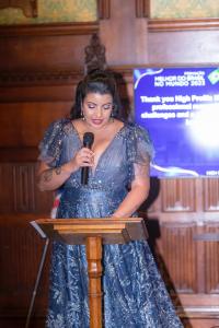 Mulher com cabelos longos escuros, discursando em um púpito, maquiada e usando batom vermelho