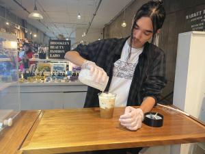 A young man pouring a banana milk mixture from a blender into a cup.