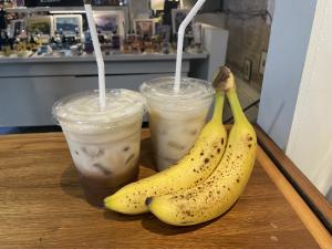 Two drinks on a wooden table, one behind the other, posed next to a banana bunch.