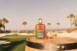 Chicken Cock Whiskey Kevin Kisner Reserve Cask Bottle sitting on a barrel in the golf course with palm trees in the background