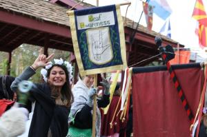 Picture of woman signing "I love you" using the ILY sign in American Sign Language. She is standing in front of a flag with the same hand sign that says Deaf Awareness. The caption for the image is: Texas Renaissance Festival will host two Deaf Awareness 