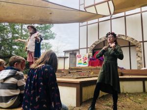 Picture of a man acting on stage wearing Renaissance clothing with a young woman standing next to the stage interpreting what he is saying in American Sign Language. The caption reads: Texas Renaissance Festival will host two Deaf Awareness Weekends in 20