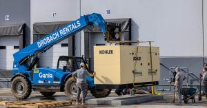 Photo of a large industrial generator being lowered onto a cement pad by a forklift