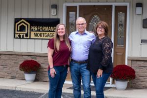 Photo of KTL Performance Mortgage ownership team in front of Greenville office. Shown are Desteni Mason, John Heath, and Kristina Heath. They are standing in front of a tan office building. The KTL Performance Mortgage sign is visible in the background,