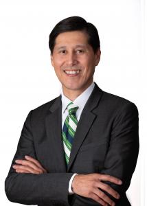 A headshot of Juan Amador, the Executive Director of SACNAS.  He is a man wearing a dark gray jacket and white collared shirt and a tie with white, green, dark blue and tan diagnol stripes.  He has black hair and is crossing his arms in front of his chest