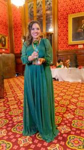 Mayara Marinov no Palácio  do Parlamento Britânico com seu troféu de vencedora. com vestido longo verde e trofeiu verde e amarelo