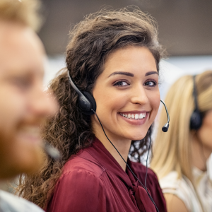 Image of a female customer service employee with a headset on smiling at the camera as she answers questions at Rosemark's home care management software