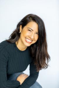 A photo of Anika Jackson, smiling with head tilted with long straight brown hair, in a black long sleeved top.