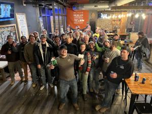 Large group of people standing in an axe throwing bar, wearing holiday colors and sweaters