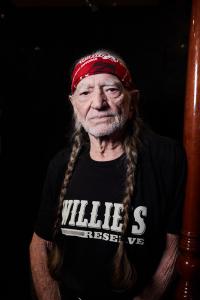 Musician Willie Nelson, with long red hair braids wearing a Willie's Reserve t-shirt in black.
