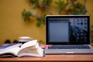 Open book next to a laptop on a wooden surface.