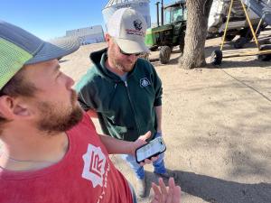 A cattle farmer showing his Cattler app on the phone to another farmer
