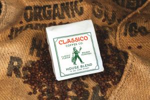 A white bag of coffee on top of a burlap coffee bag. The logo of Classico Coffee appears on the bag.