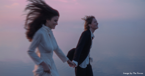 Wedding portrait of couple holding hands and running by the water with a pastel sunrise