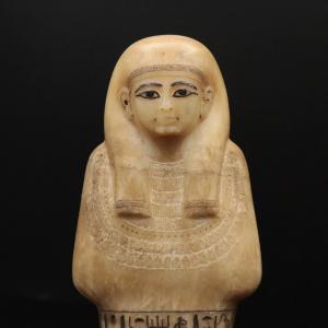 The face of the Shabti; a round face with delicate features, a heavy wig over both shoulders, and a large beaded collar around his neck