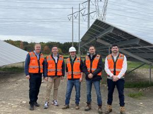 Five men in safety vests posing for photo in solar field.