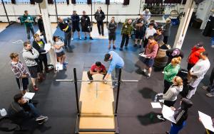 A group of attendees look on as Matt Reynolds teaches the squat at a Barbell Logic seminar